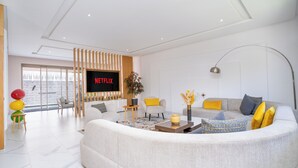 A modern living room with a large sofa, a TV displaying 'NETFLIX,' and a large window.