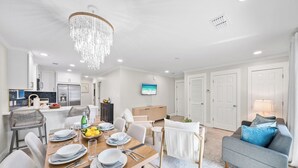 Uma sala de estar moderna e bem iluminada, com área de jantar, cozinha e TV na parede.