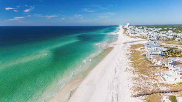 Vista aérea de uma área costeira com praia, casas e um farol.