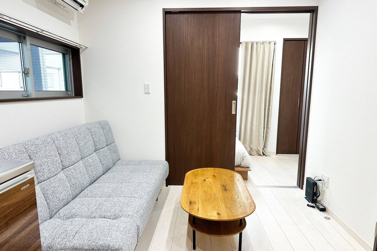 A room with a grey sofa, a wooden coffee table, and a wooden door leading to another room.