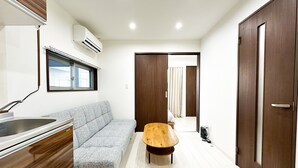 Una sala moderna con un sofá gris, una mesa de centro de madera, una zona de cocina con un fregadero y un ventanal grande.