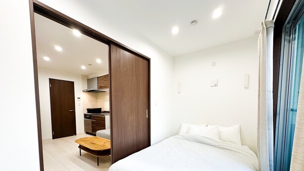 Un dormitorio moderno con una cama grande, un banco de madera y una kitchenette al fondo.
