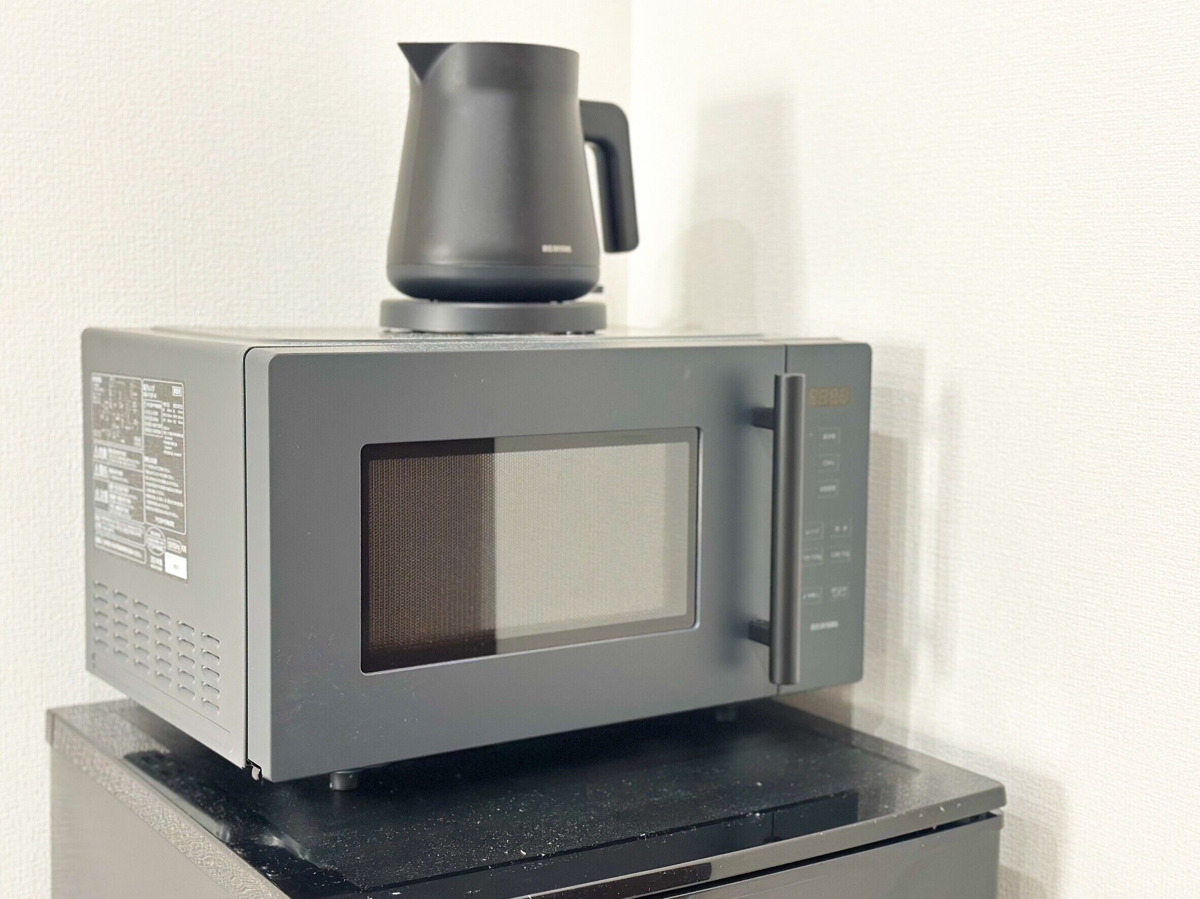A microwave oven with a black coffee pot on top, placed on a black countertop.