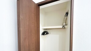 Una puerta de madera que da a una habitación con pared blanca, un perchero metálico y un estante blanco.