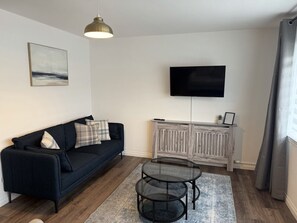 A living room with a sofa, a glass coffee table, a mounted TV, and a radiator.