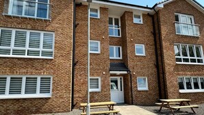 A two-story brick building with multiple windows and a central door. There are two picnic tables in the courtyard. - 0/2 Inchcruin Apartment  - Macaulay Letting (Bonhill)