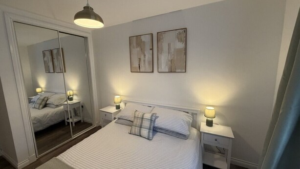 A bedroom with a bed, bedside tables, a mirror, and artwork on the wall. - 0/2 Inchcruin Apartment  - Macaulay Letting (Bonhill)