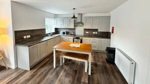 A modern kitchen with white cabinets, a wooden table, and a black trash bin. - Inchconnachan Apartment (Bonhill)