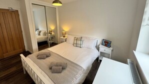 A bedroom with a bed, bedside tables, a mirror, a wardrobe, and a radiator. - Inchconnachan Apartment (Bonhill)