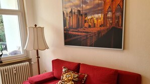 A red sofa with a floral pillow, a radiator, a lamp, and a cityscape painting on the wall. - Temporary living  (Freiburg im Breisgau)