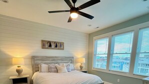 A bedroom with a bed, nightstands, a ceiling fan, and large windows.