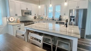 A modern kitchen with white cabinets, a large island, stainless steel appliances, and pendant lighting.
