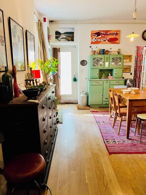 A cozy kitchen with wooden cabinets, a dining table, and chairs. There is a window with curtains, a green refrigerator, and various kitchen items on the countertops. - Charming family home near Sacré-Cœur (Ile de France, Paris)