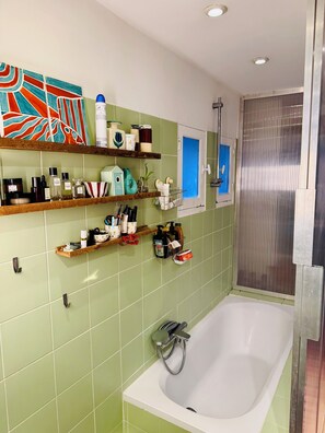 A bathroom with a bathtub, green tiled walls, and shelves with toiletries. - Charming family home near Sacré-Cœur (Ile de France, Paris)