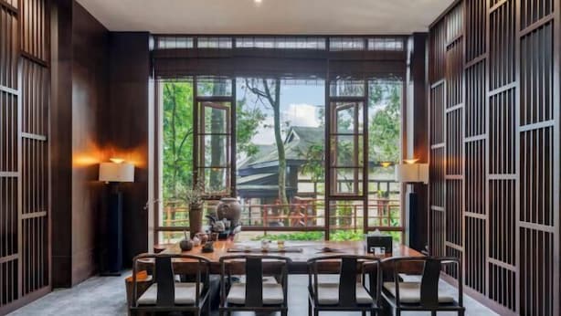 A dining area with a large table and chairs, a view of greenery outside, and traditional wooden decor. - Emei Mountain Wannian Xueya Fang Hotel (Emeishan City)