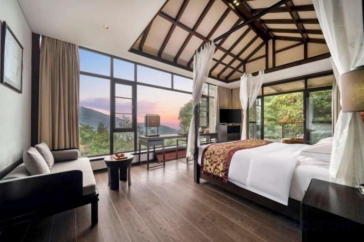 Een slaapkamer met een groot bed, een zithoek en uitzicht op het groen.