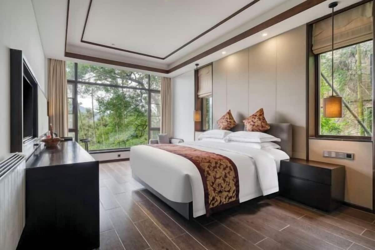 Une chambre d’hôtel moderne, dotée d’un grand lit, d’un bureau et offrant une vue sur la verdure environnante.