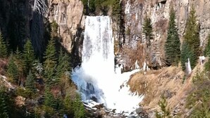 A waterfall cascading down a rocky cliff surrounded by dense forest. - Bluebird Day - Huckleberry Cottage in Bend, OR, perfect for a romantic getaway. (Bend)