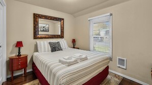 A bedroom with a bed, a nightstand, a mirror, and a window with blinds. - Bluebird Day - Huckleberry Cottage in Bend, OR, perfect for a romantic getaway. (Bend)