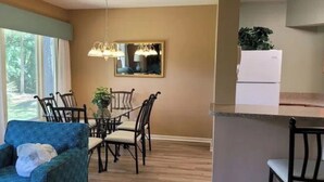 A dining area with a chandelier, a dining table with chairs, and a kitchen area with a refrigerator. - Shipyard Resort - Brigantine Quarters (Hilton Head Island)
