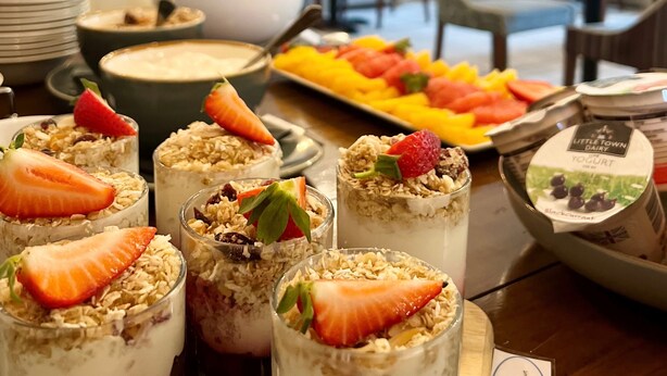 Un comedor con una mesa de buffet que ofrece diversas opciones de comida, como vasos de yogur con granola y fruta.