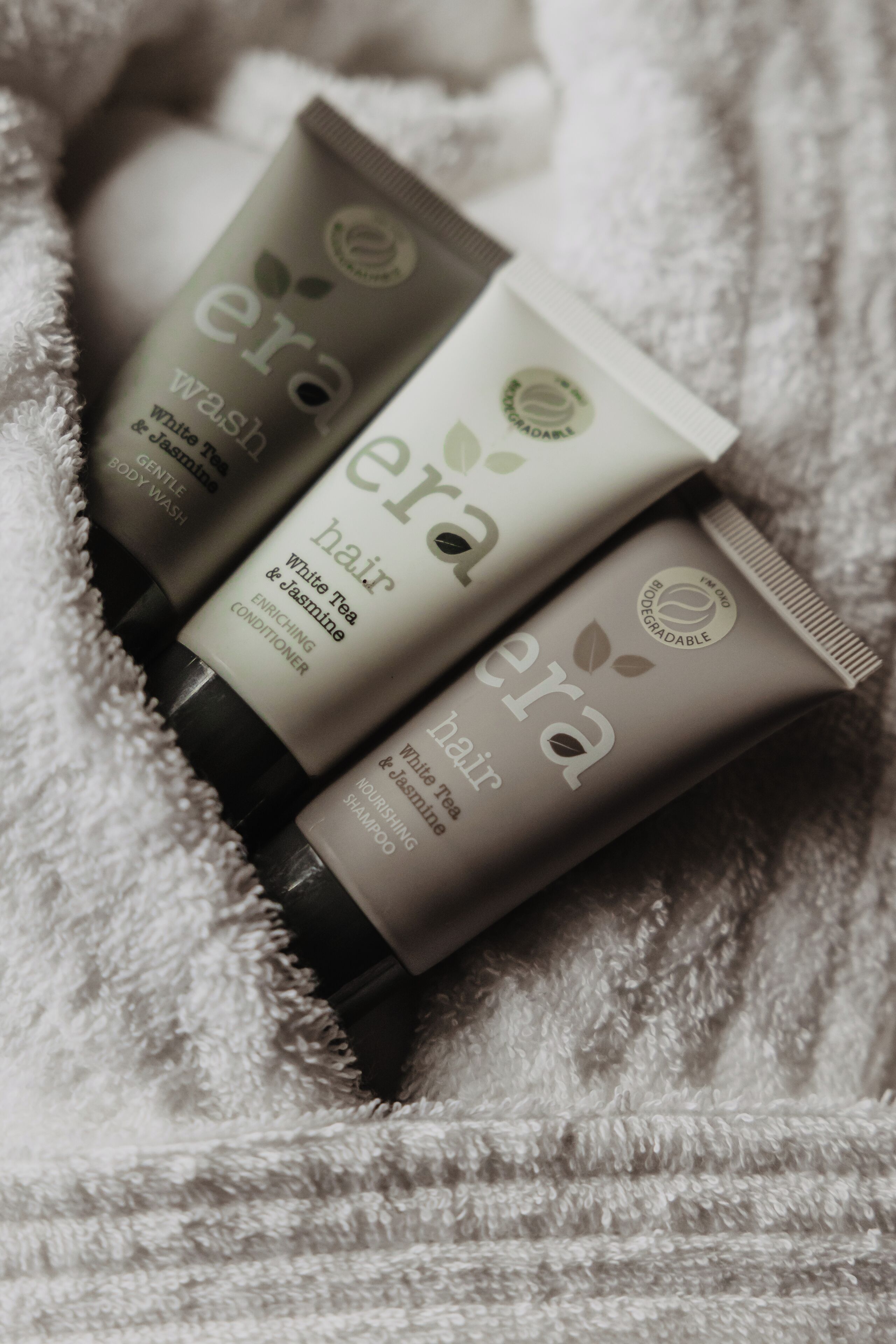 Three bottles of 'era' hair and body wash products on a white towel.