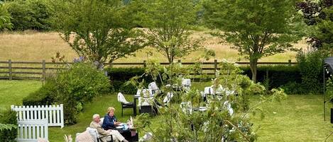 An outdoor seating area with tables and chairs, surrounded by greenery and trees.