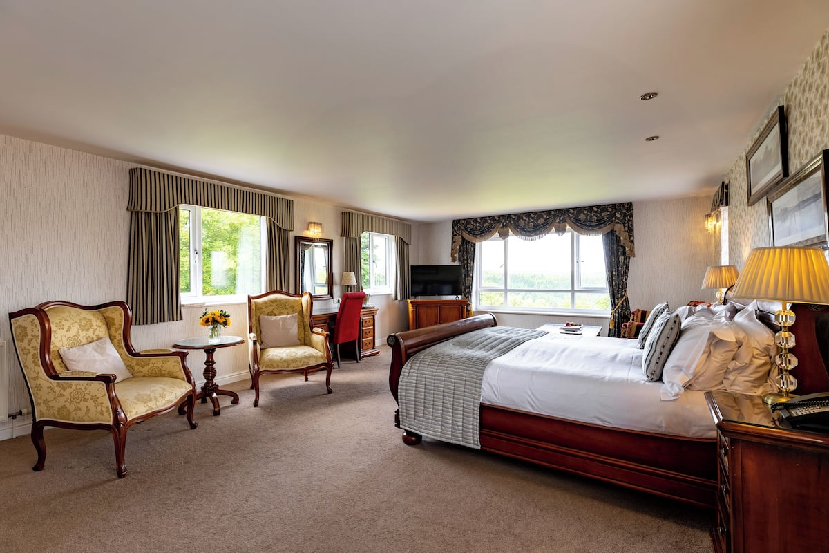 A hotel room with a large bed, two armchairs, a small table, and a TV.