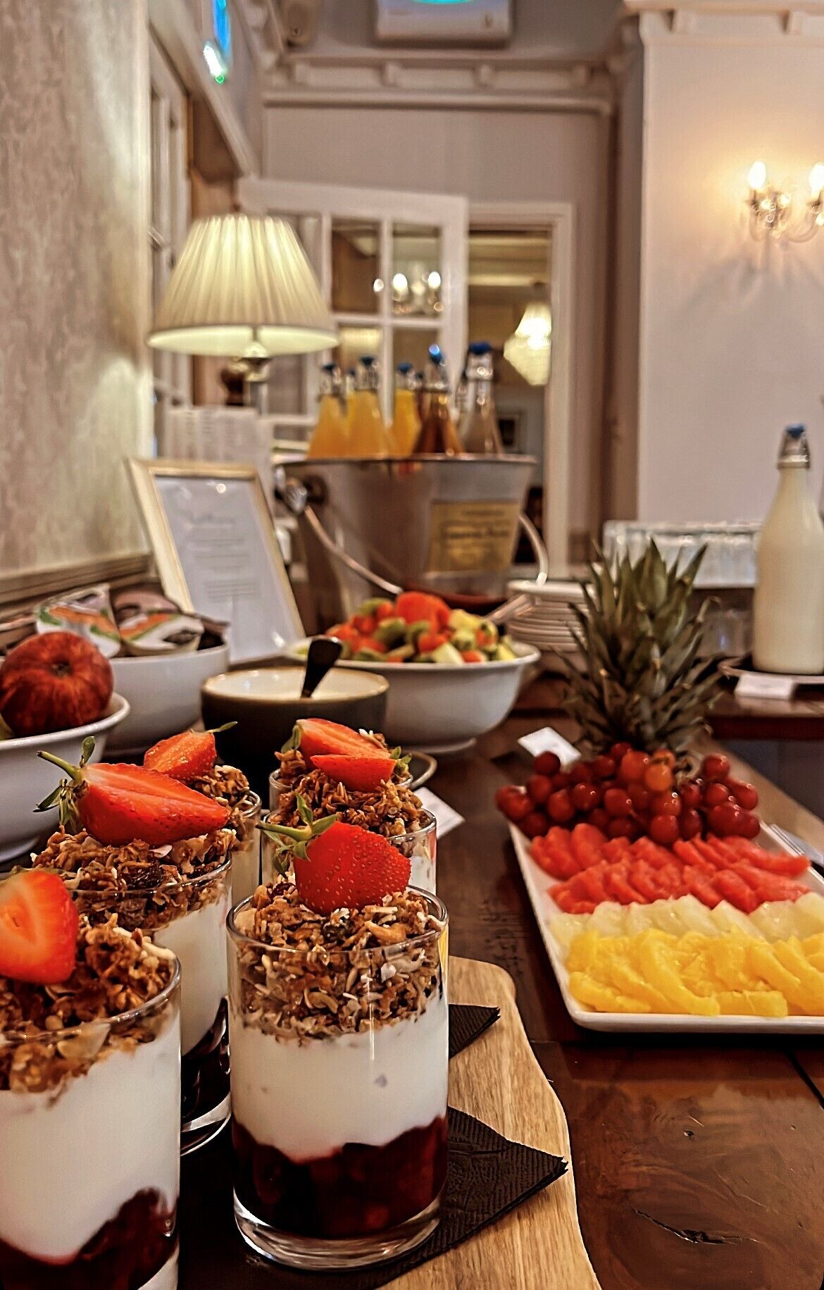 Una mesa de comedor con diversos alimentos, incluyendo fruta, una piña y un postre con fresas y granola.