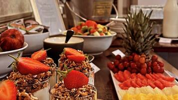 Una mesa de comedor con diversos alimentos, incluyendo fruta, una piña y un postre con fresas y granola.
