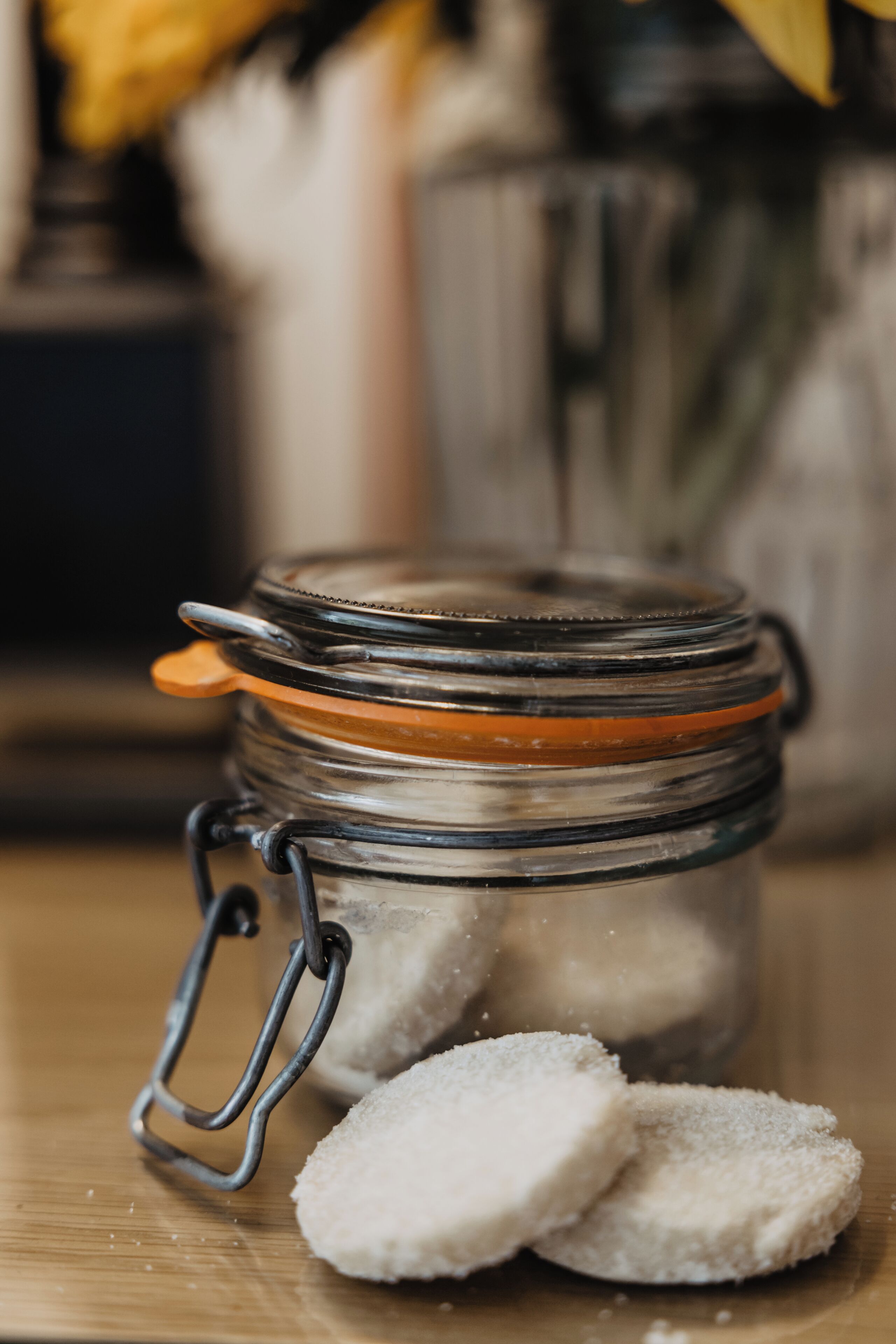 Un bocal en verre doté d’un couvercle à fermoir métallique et d’un anneau métallique, contenant une substance blanche et granuleuse, posé sur une surface en bois.