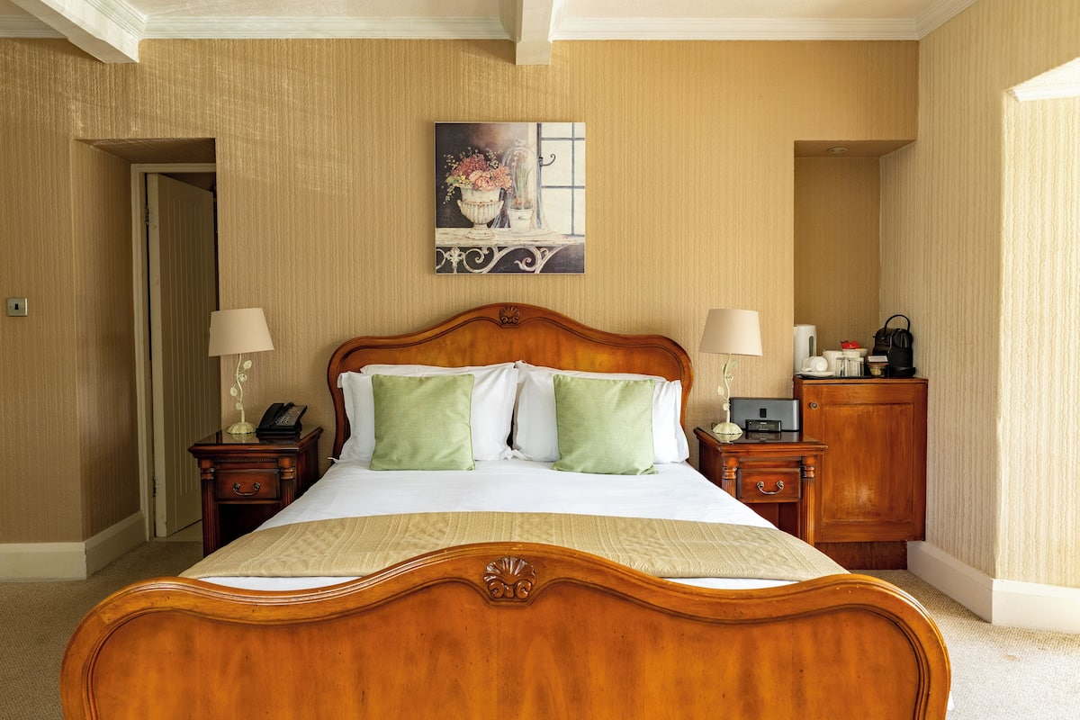 A hotel room with a wooden bed, two bedside tables with lamps, a nightstand, a dresser, and a painting on the wall.