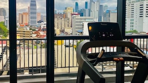 A view from a balcony with a treadmill, overlooking a cityscape with high-rise buildings and a prominent tower.