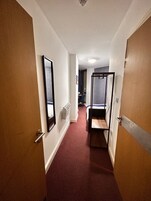 Un pasillo estrecho con una alfombra roja que conduce a una habitación con una cama y una mesita.