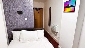 A hotel room with a bed, a headboard, a wall-mounted air conditioner, a door, and a framed picture of a city skyline. - Hillcrest Liverpool Central (Liverpool)