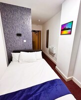 Una habitación de hotel con cama, cabecera, aire acondicionado de pared, puerta y un cuadro enmarcado con una vista del horizonte urbano.