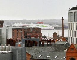 Vista de una zona costera con edificios, un barco grande atracado en el puerto y una chimenea alta.