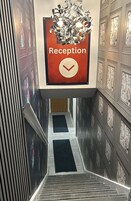 Zona de recepción con un cartel que indica la ubicación, una escalera que sube a un piso superior y paneles decorativos en la pared.