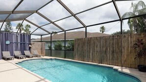 Una piscina con techo de estructura geométrica, rodeada de sillas de descanso y una valla de bambú.