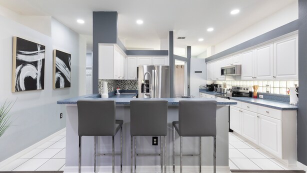 Una cocina moderna con armarios blancos, una isla central con taburetes altos, electrodomésticos de acero inoxidable y un salpicadero con diseño geométrico.