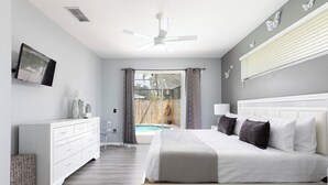 Un dormitorio con cama, cómoda, ventilador de techo, televisor y vista a una piscina.
