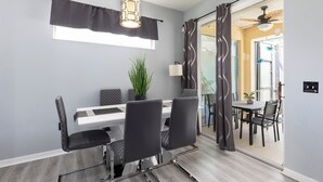 Comedor con mesa blanca, sillas negras, lámpara colgante y planta en maceta.