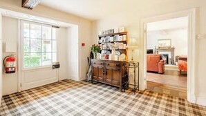 A room with a checkered floor, a wooden cabinet with decorative items, a fire extinguisher, and a door leading to another room.