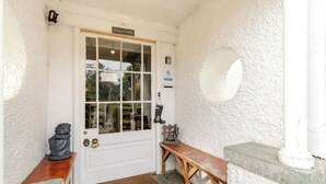 A white door with a 'WELCOME' sign, a bench, a small table, and a round window on the wall.