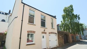A two-story building with a beige facade, a brick archway entrance, and a small window with shutters. - Coach House in Clifton village (Bristol City)