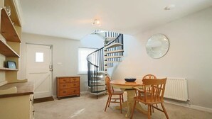 A dining area with a round table and chairs, a spiral staircase, and a radiator on the wall. - Coach House in Clifton village (Bristol City)