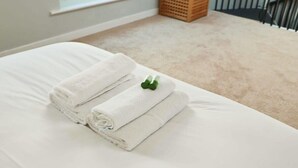 A neatly made bed with folded white towels and a green bottle on it. - Coach House in Clifton village (Bristol City)