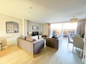 Ein modernes Wohnzimmer mit Sofa, Fernseher und einem Essbereich mit Stühlen.