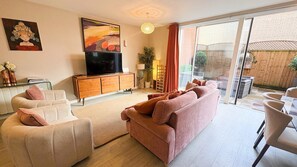 Un salon comprenant un canapé, des fauteuils, un téléviseur et une porte-fenêtre coulissante donnant sur un espace extérieur.