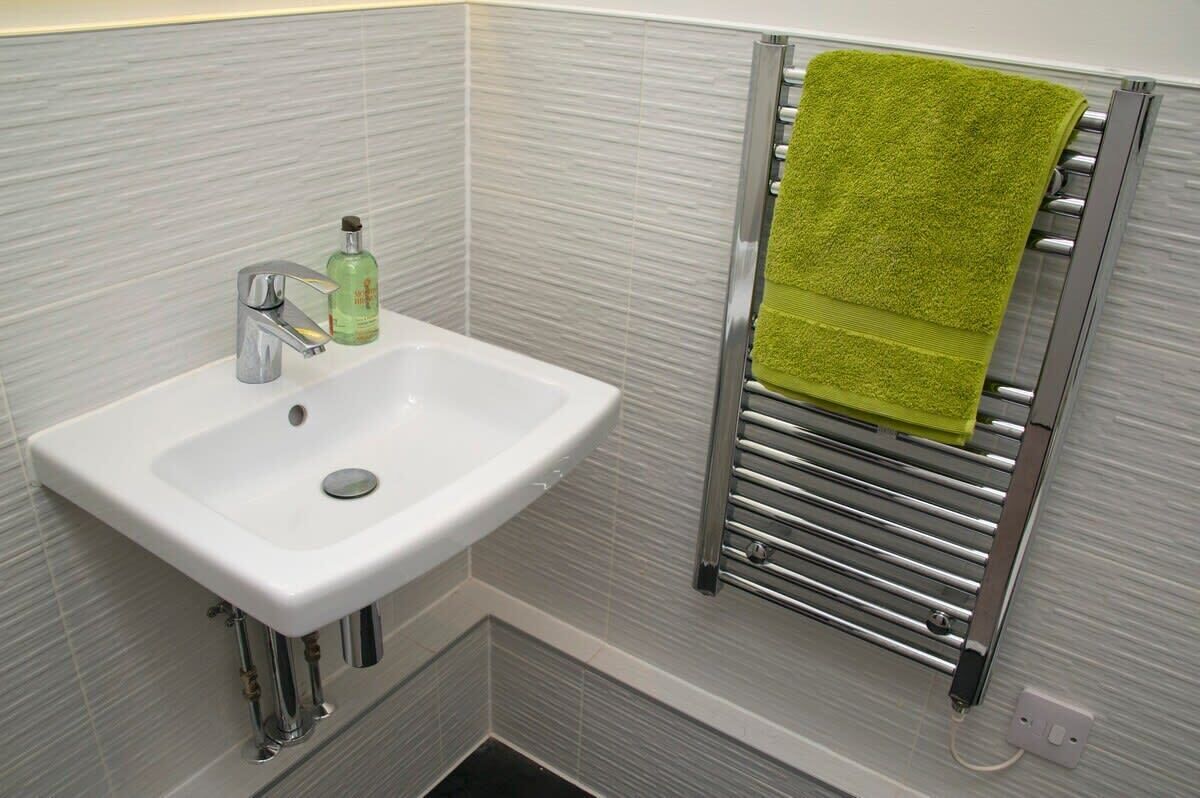Un baño con un lavamanos blanco, grifo cromado y un toallero con una toalla verde.